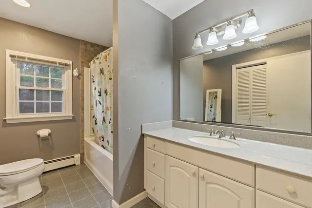 a bathroom with a sink a toilet a mirror a window and shower