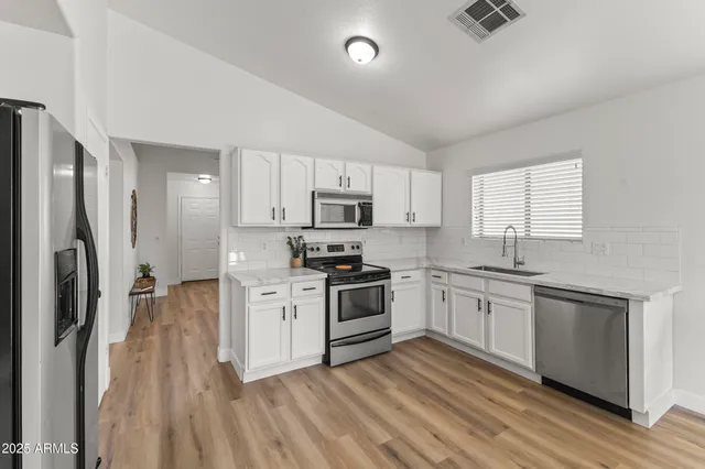 a kitchen with stainless steel appliances granite countertop a stove a sink dishwasher a refrigerator and white cabinets with wooden floor