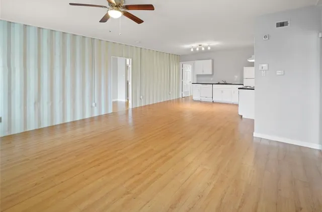 a view of an empty room with wooden floor and a ceiling fan