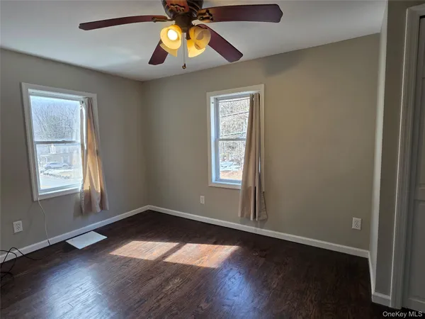an empty room with wooden floor chandelier fan and windows