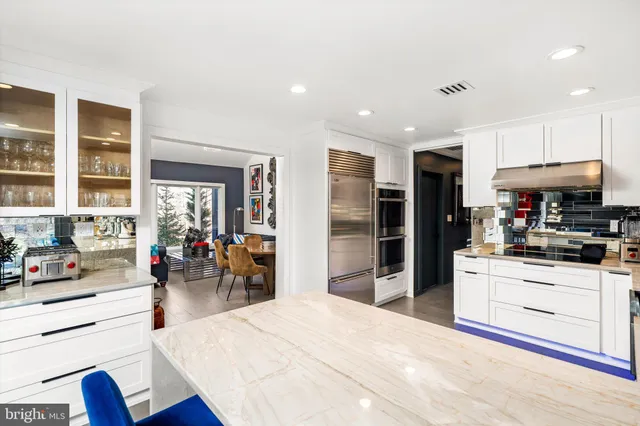 a kitchen with stainless steel appliances kitchen island granite countertop a refrigerator oven stove a dining table and chairs with wooden floor