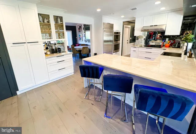 a kitchen with stainless steel appliances kitchen island granite countertop a refrigerator a stove a sink a dining table and chairs with wooden floor