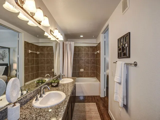 a bathroom with a granite countertop sink a mirror a bathtub and shower