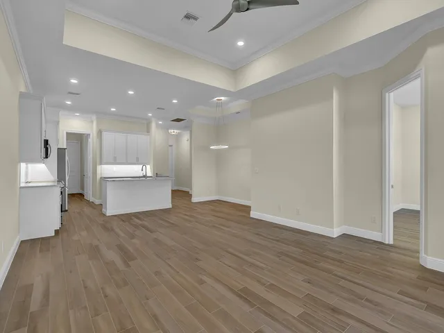 a view of an empty room with wooden floor and a kitchen