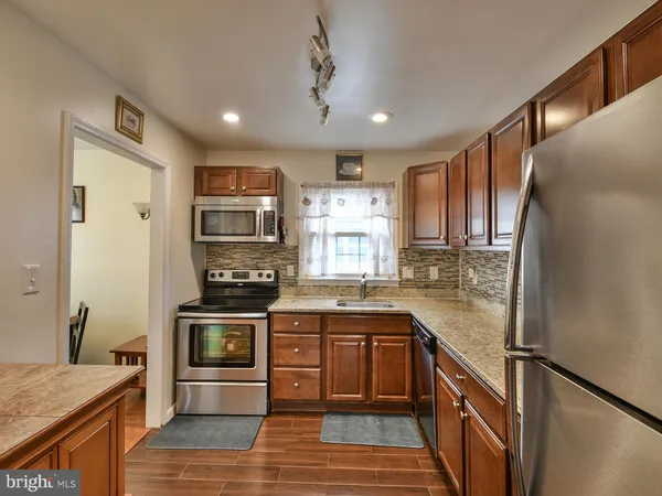 a kitchen with stainless steel appliances granite countertop a stove top oven a sink dishwasher a refrigerator and a dining table with wooden floor