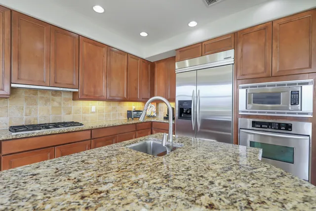 a kitchen with stainless steel appliances granite countertop a refrigerator a stove and a sink with wooden cabinets