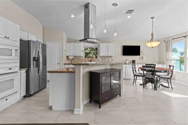 a kitchen with stainless steel appliances granite countertop a stove top oven a refrigerator and a dining table with a kitchen island