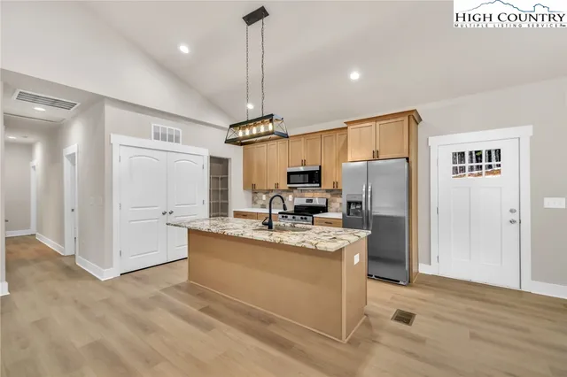a view of a kitchen with kitchen island a refrigerator wooden floor and a view of living room