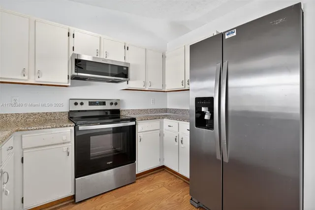 a kitchen with stainless steel appliances granite countertop a refrigerator a stove and white cabinets