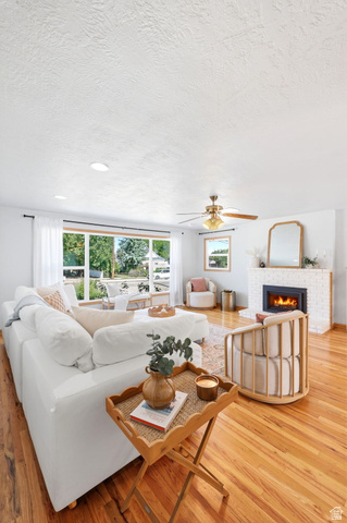 1180 North 400 East Bountiful, UT 84010 - Photo 12 of 50 Spacious living area featuring expansive windows, wood-finish flooring, a white brick fireplace with a black insert, and a ceiling fan with integrated lighting