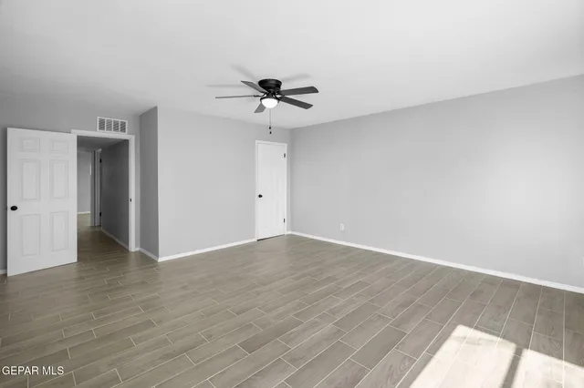 a view of an empty room with wooden floor and a ceiling fan
