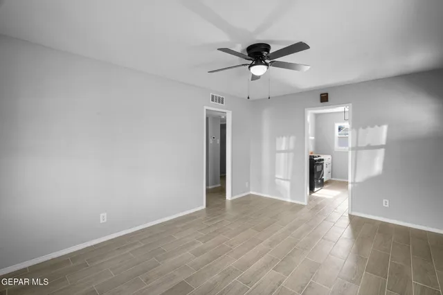 a view of an empty room with wooden floor and a ceiling fan
