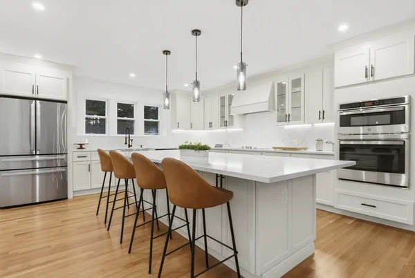 a kitchen with stainless steel appliances granite countertop a stove a sink a microwave a refrigerator and white cabinets with wooden floor