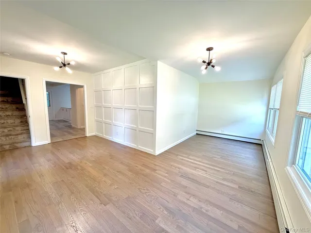 an empty room with wooden floor and way to kitchen