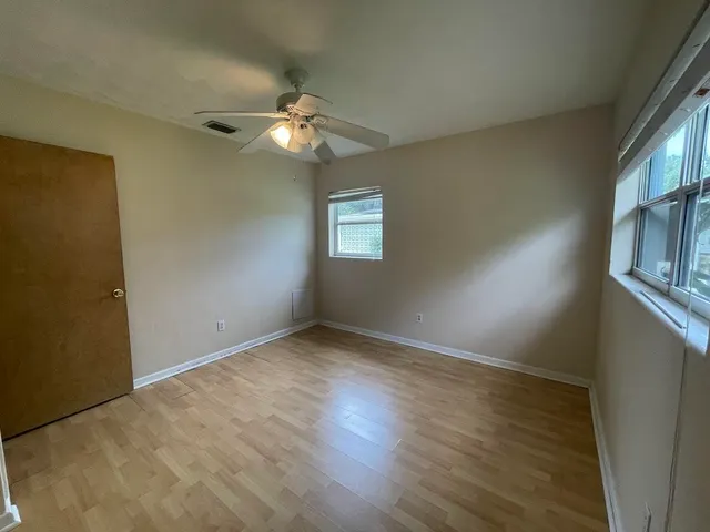 an empty room with wooden floor fan and windows