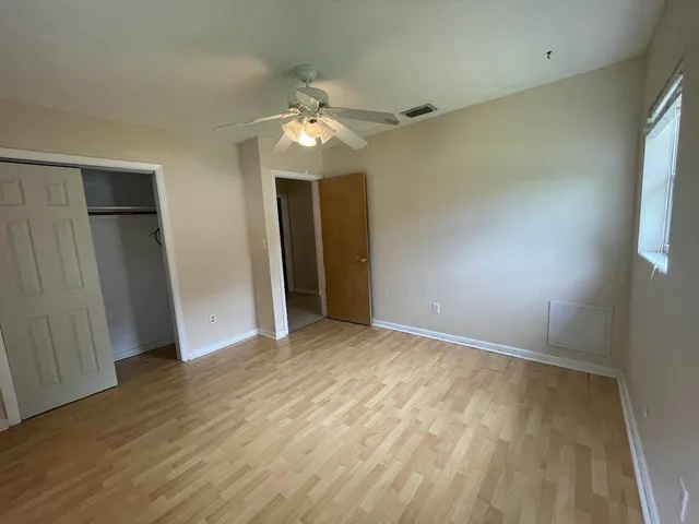 an empty room with wooden floor fan and windows