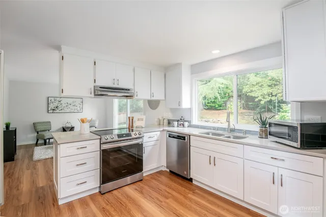 a kitchen with white cabinets appliances a sink and a window