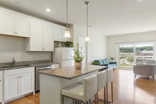 a kitchen with kitchen island granite countertop a table chairs sink and white cabinets with wooden floor