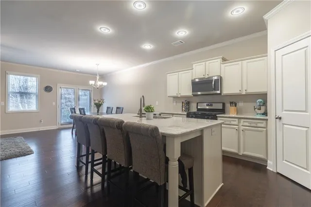 a kitchen with stainless steel appliances a stove a sink a refrigerator cabinets and a dining table with wooden floor