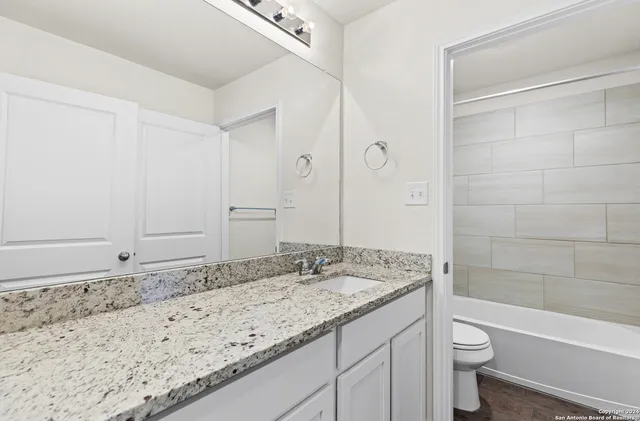 a bathroom with a granite countertop sink a toilet a shower and a mirror