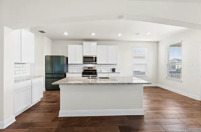 a kitchen with stainless steel appliances granite countertop a refrigerator a stove a sink and white cabinets with wooden floor