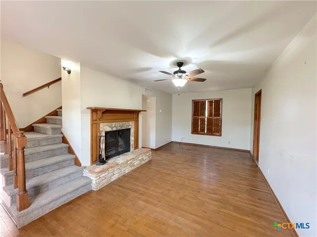 a view of an empty room with wooden floor fireplace and a window