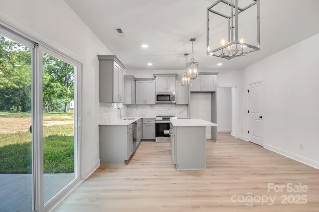 a large kitchen with stainless steel appliances kitchen island granite countertop a large kitchen island a stove a refrigerator a sink and a large window