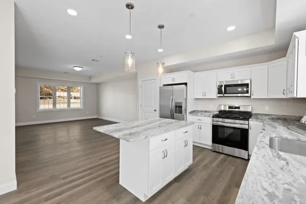 a kitchen with stainless steel appliances granite countertop a stove a sink a refrigerator white cabinets and wooden floor