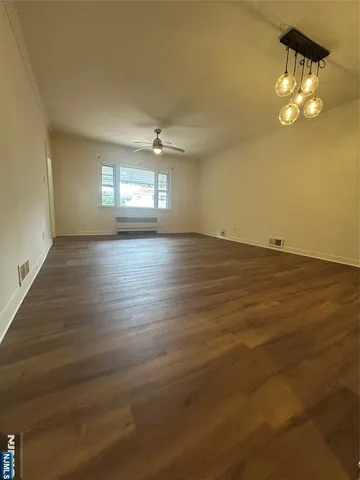 an empty room with wooden floor chandelier and windows
