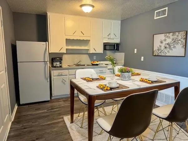 a white kitchen with a stove a refrigerator a sink a dining table and chairs