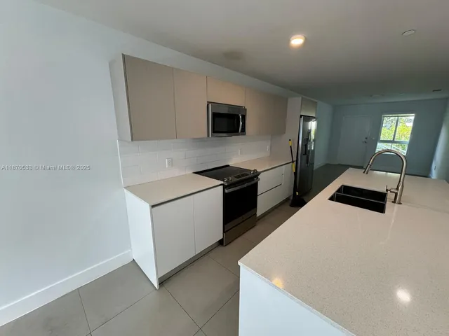 a kitchen with stainless steel appliances a stove top oven a sink a refrigerator and white cabinets