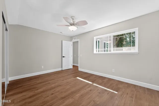 an empty room with wooden floor ceiling fan and window