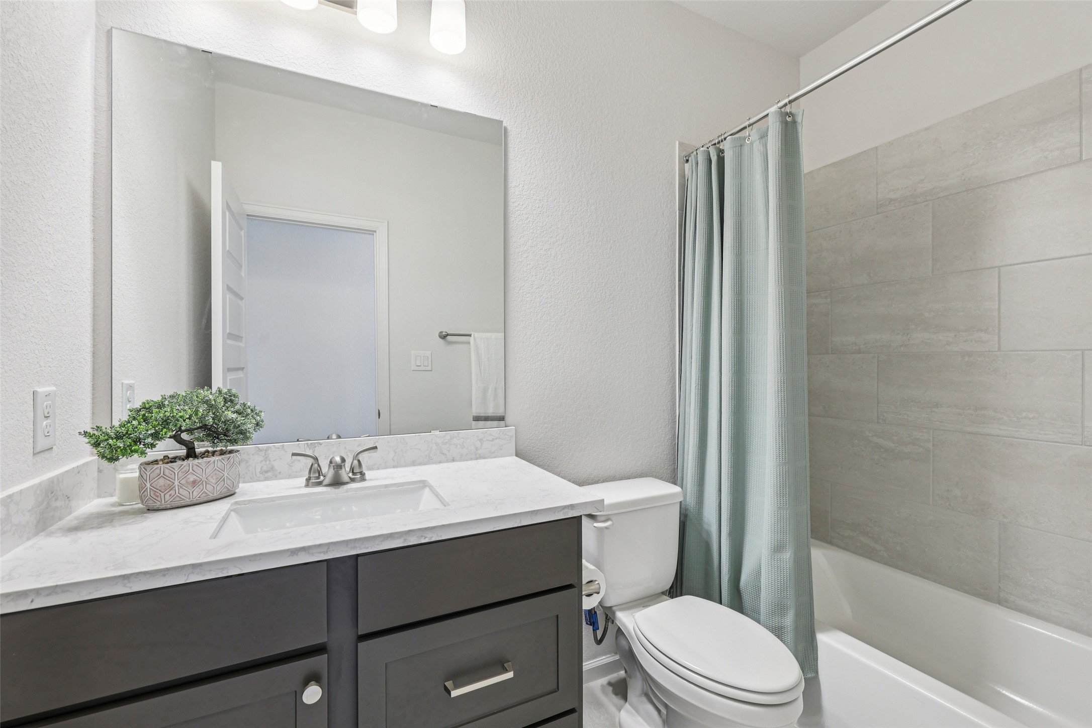 1140 Bryson Rdg Trail Leander, TX 78641 - Photo 27 of 39 Well-appointed bathroom featuring a vanity with a white countertop and a rectangular undermount sink, a large mirror, and a bathtub with light gray tiled walls
