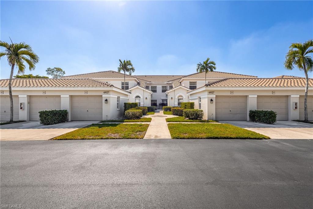 View of front of house with a front yard, stucco siding, a tile roof, and community garages