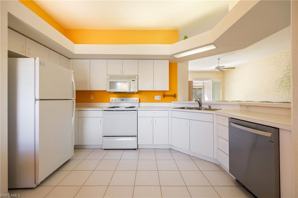 6927 Satinleaf Road North, Unit 203 Naples, FL 34109 - Photo 10 of 39 Kitchen with white appliances, light countertops, white cabinets, light tile patterned flooring, and a peninsula