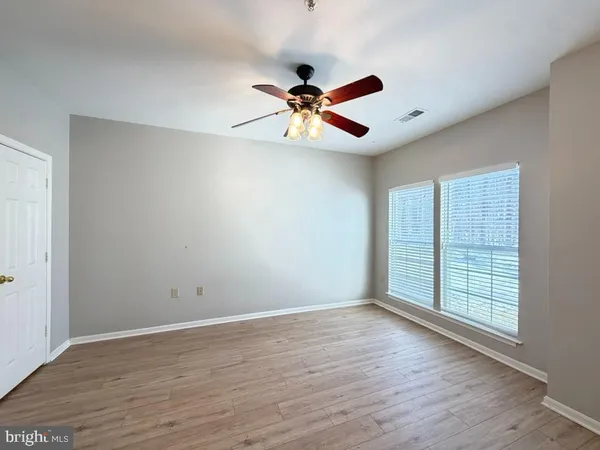 an empty room with wooden floor fan and windows