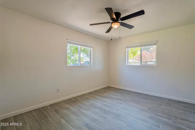 an empty room with wooden floor ceiling fan and windows