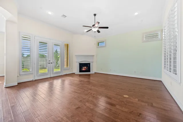 an empty room with wooden floor chandelier fan and windows