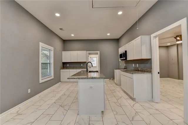 a kitchen with granite countertop kitchen island a sink stainless steel appliances and white cabinets