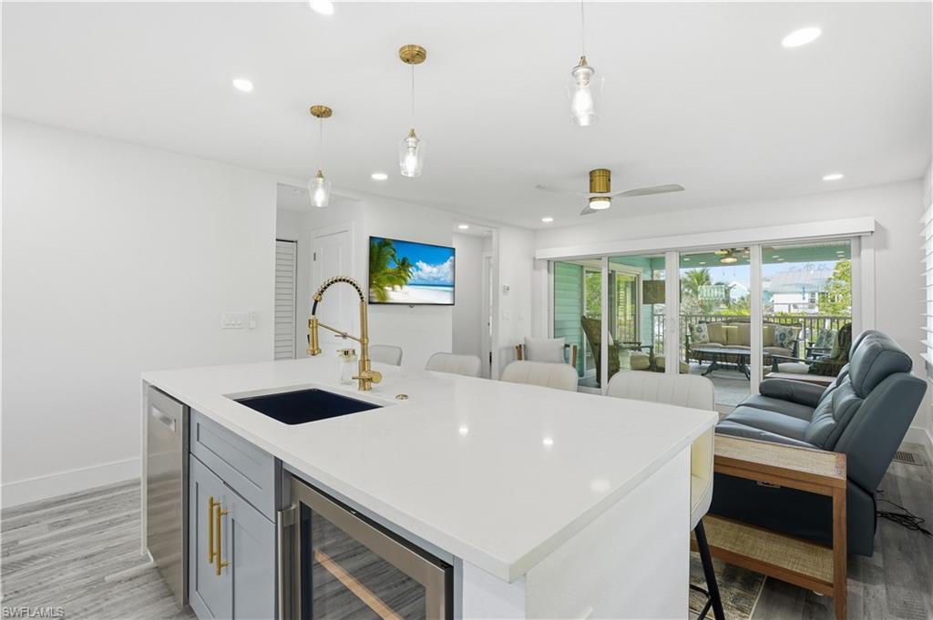 270 Dundee Road Fort Myers Beach, FL 33931 - Photo 11 of 48 Kitchen with light wood finished floors, beverage cooler, hanging light fixtures, open floor plan, and light stone countertops - Virtually Edited Image