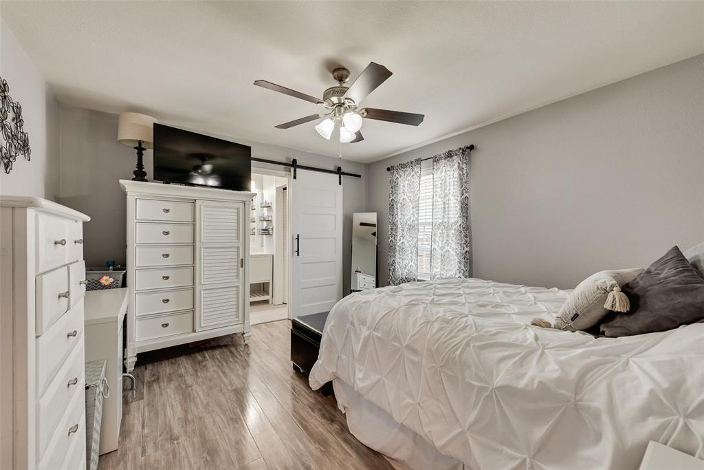149 Cattlemans Creek Road Newark, TX 76071 - Photo 15 of 39 Primary bedroom with laminate floors, ceiling fan and barn door to ensuite bathroom at 149 Cattlemans Creek Rd in the Chisholm Springs neighborhood in Newark, TX 76071
