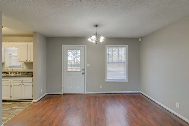 an empty room with wooden floor chandelier and windows