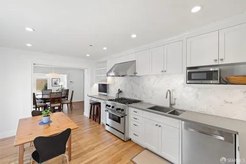 a kitchen with stainless steel appliances kitchen island granite countertop a sink dishwasher stove and white cabinets with wooden floor