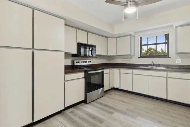 a kitchen with stainless steel appliances granite countertop white cabinets a sink a stove a dining table and chairs