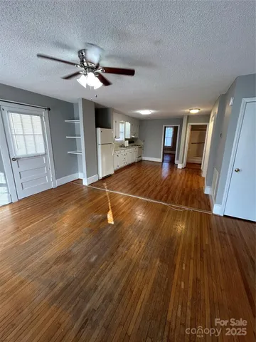 a view of an empty room with wooden floor and a ceiling fan