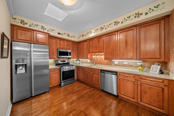 a kitchen with stainless steel appliances granite countertop a refrigerator a sink dishwasher a stove and white countertops with wooden floor
