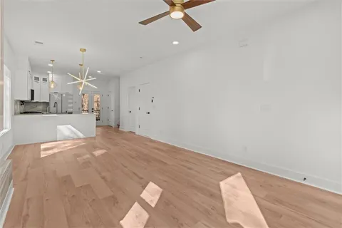 an empty room with kitchen view and a chandelier fan