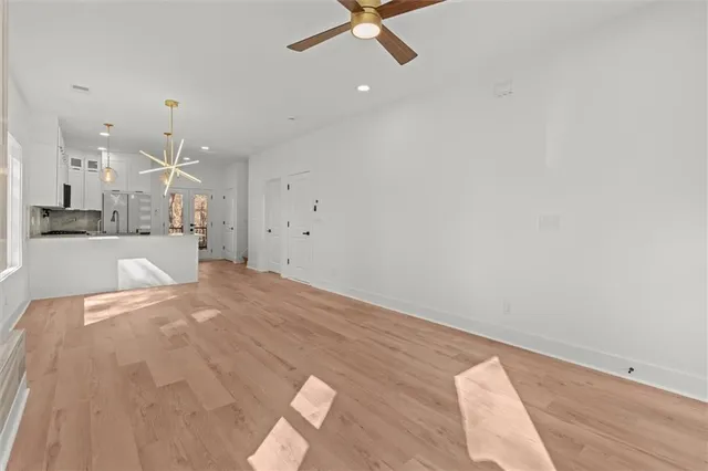 an empty room with kitchen view and a chandelier fan