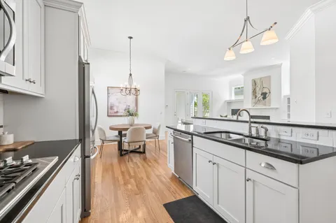 a kitchen with granite countertop a refrigerator a sink dishwasher a stove and white cabinets with wooden floor