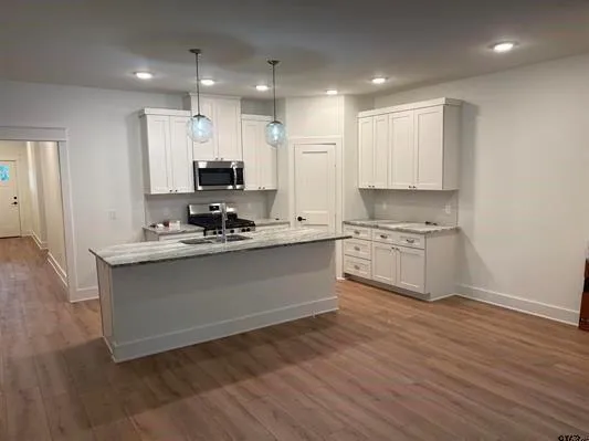 a room with kitchen island granite countertop a sink cabinets and wooden floor